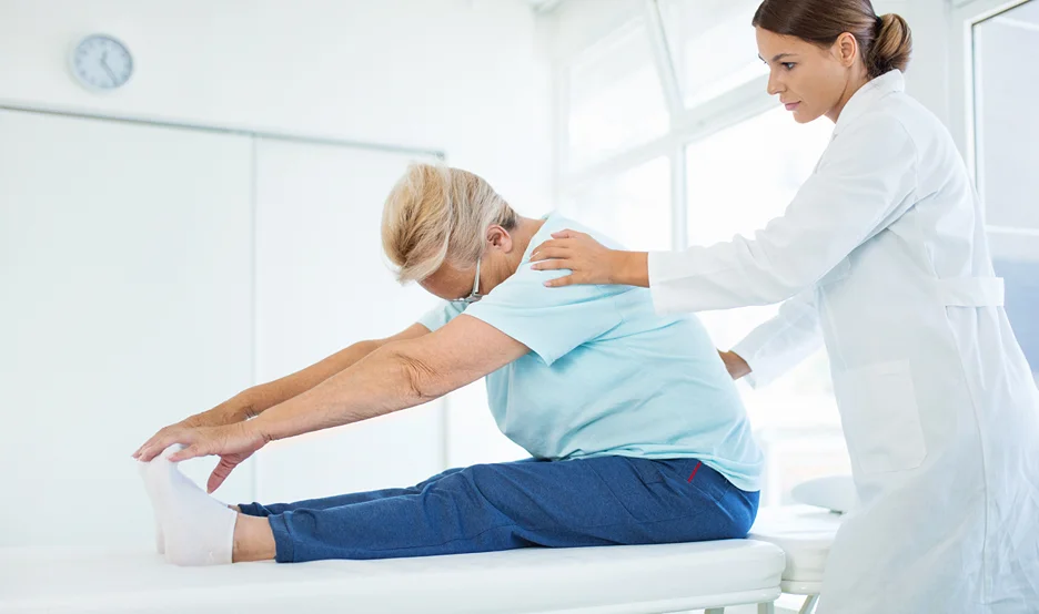 physical therapist assists her senior patient perform seated hamstring stretch