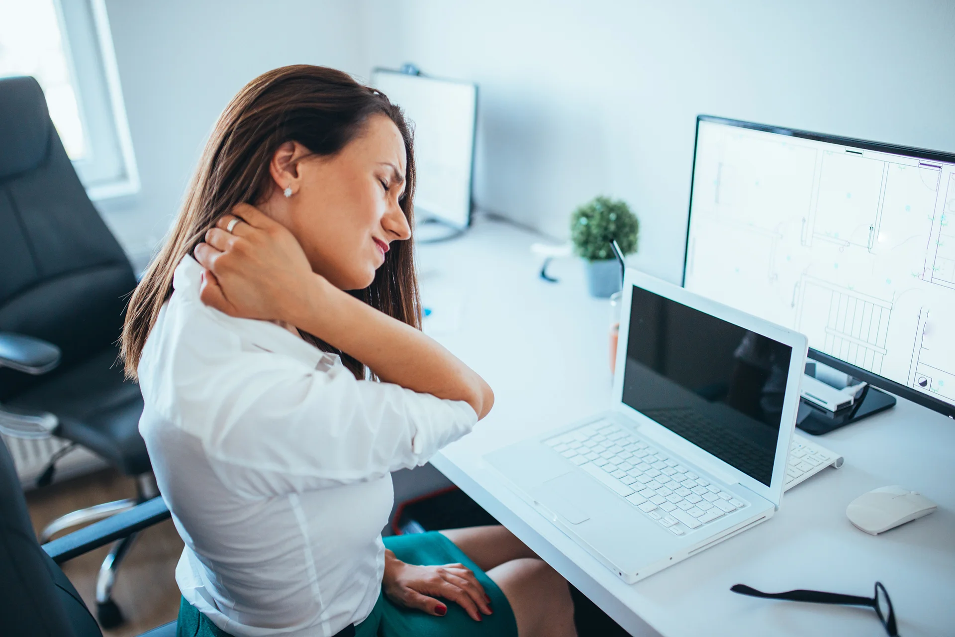 a woman tilting her pained neck while sitting inside her office