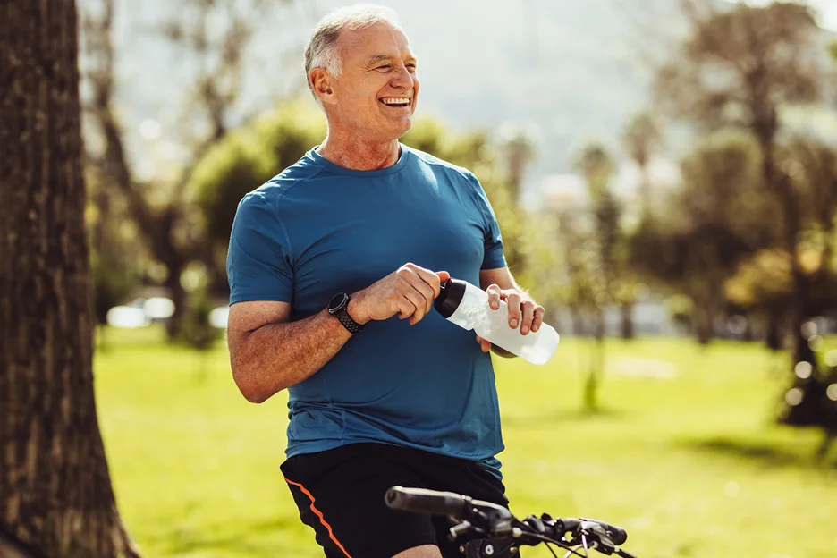 a smiling mature man sitting on his bicycle while holding a water bottle