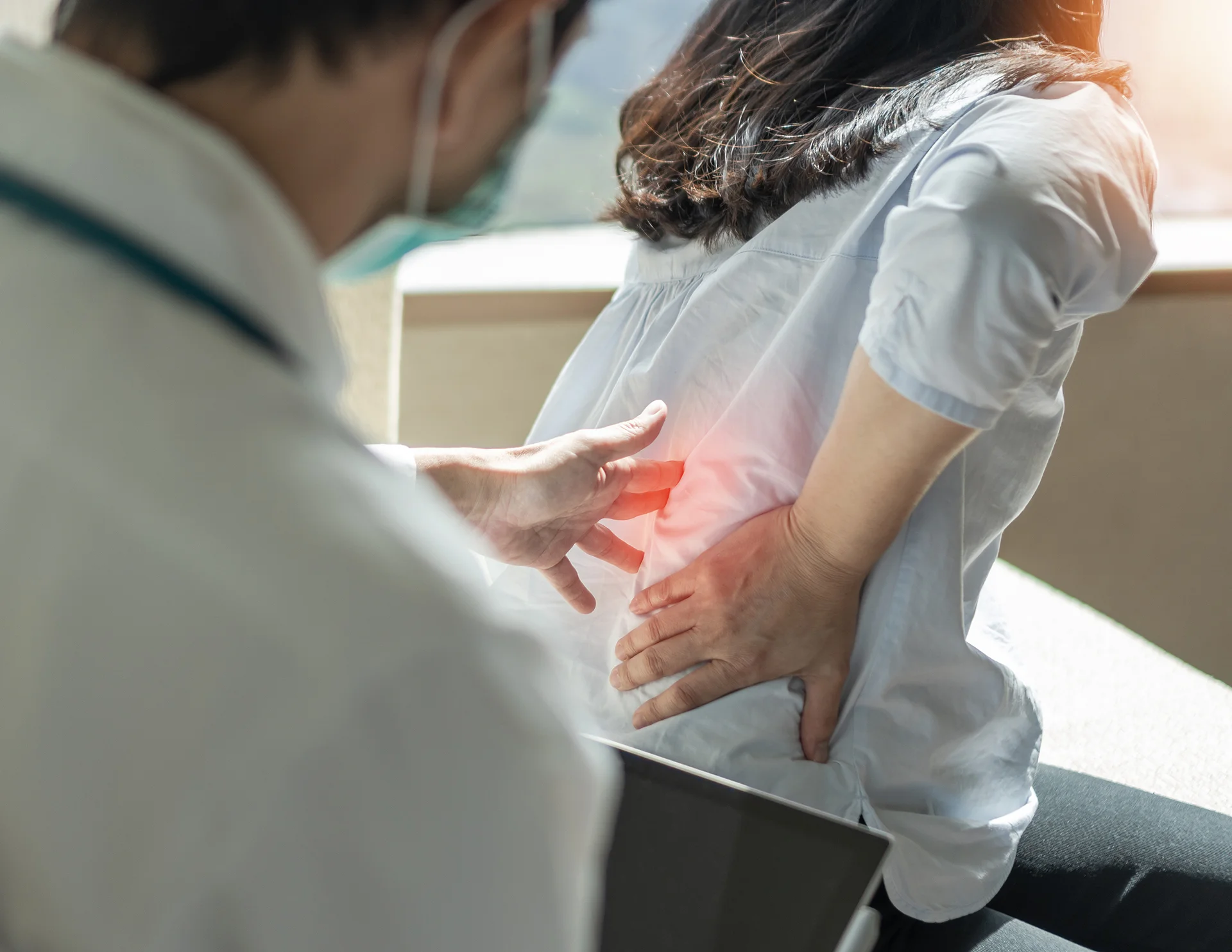 a doctor checks female patient's lower back pain issues