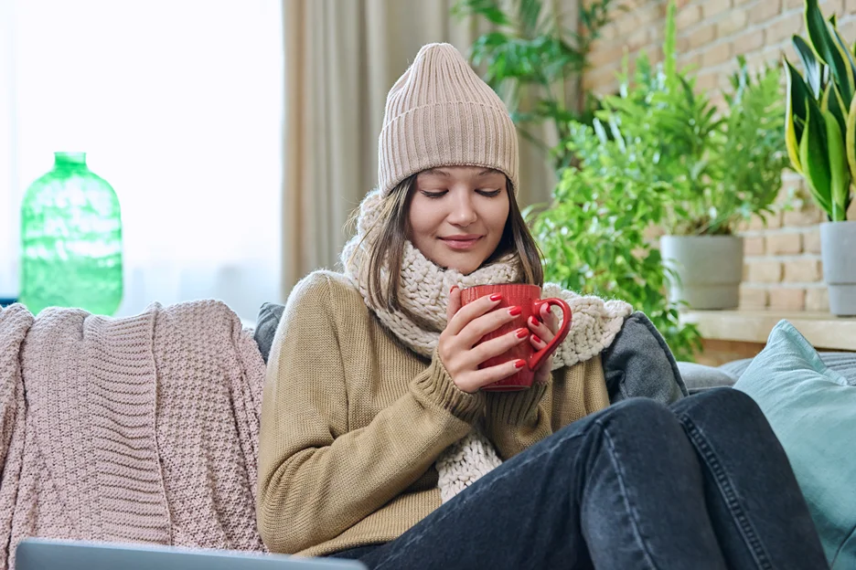 a woman wearing layered clothing during winter while holding a cup of hot beverage