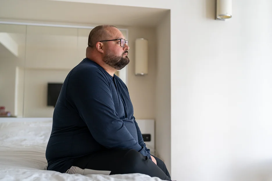 an obese man sitting on the bed